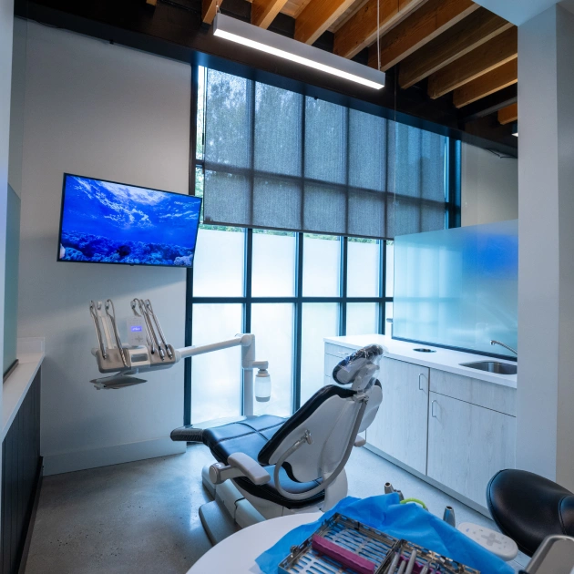 Modern dental operatory with chair, mounted monitor, and bright windows in contemporary clinic.