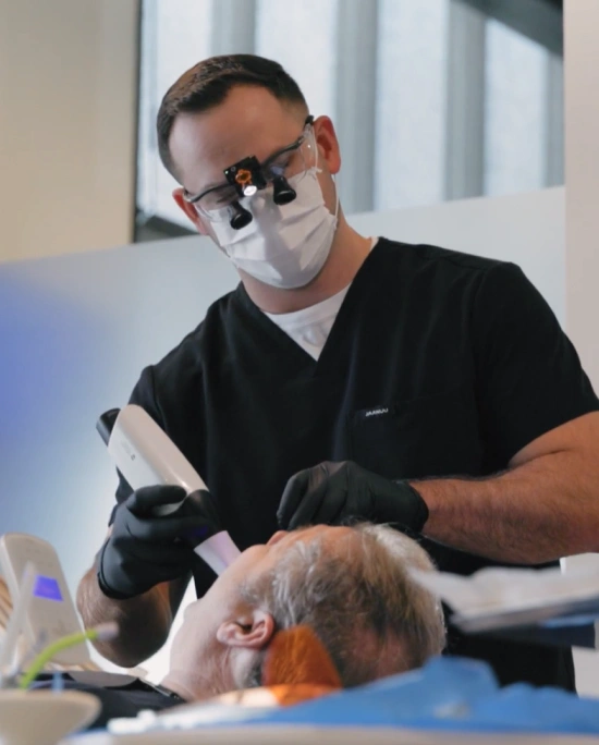 Dentist in protective mask and gloves examining elderly patient in dental office setting.